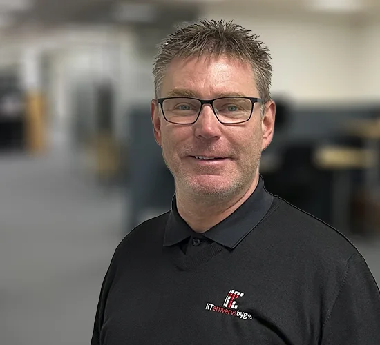 Portræt af en mand med briller og sort poloshirt med KT Erhvervsbyg A/S-logo