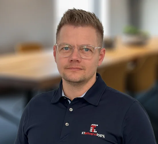 Mand med kort hår og briller i mørkeblå poloshirt med logo fra KT Erhvervsbyg A/S