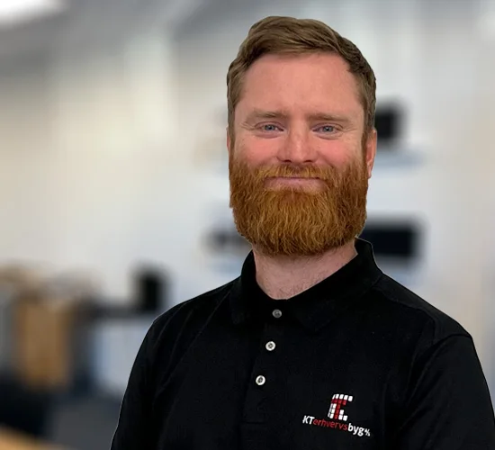 Smilende mand med rødt skæg i sort poloshirt med logo fra KT Erhvervsbyg A/S