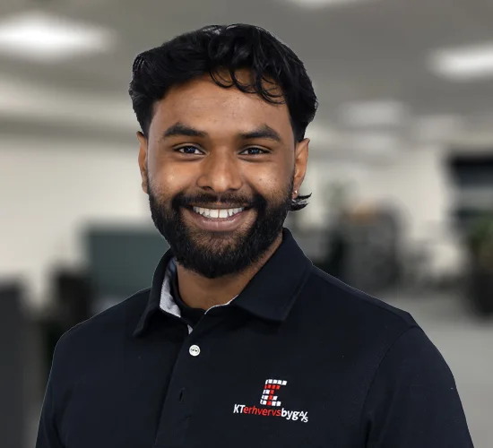 Smilende mand med mørkt hår og skæg i sort poloshirt med logo for KT Erhvervsbyg A/S