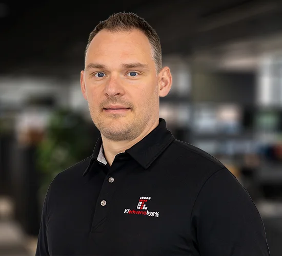 Mand i sort poloshirt med logo fra KT Erhvervsbyg A/S foran en sløret kontorbaggrund