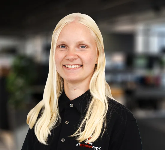 Smilende kvinde med langt, lyst hår og sort skjorte med logo for KT Erhvervsbyg A/S