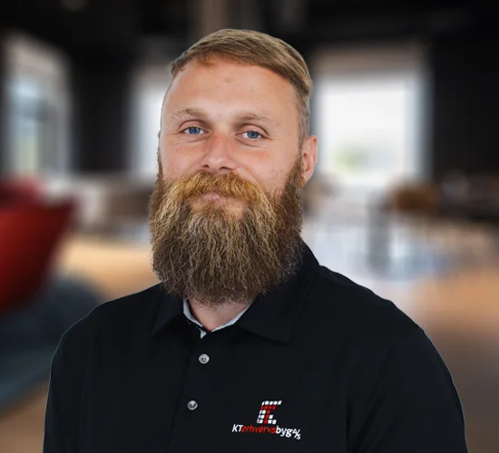 Mand med kort hår og langt skæg i sort poloshirt med logo fra KT Erhvervsbyg A/S