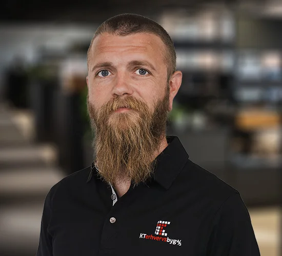 Mand med langt skæg i sort poloshirt med logo fra KT Erhvervsbyg A/S