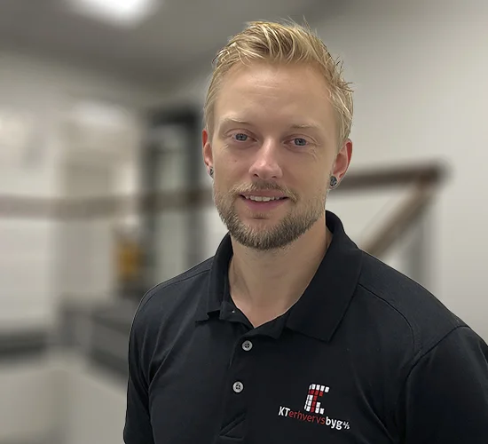 Mand med kort lyst hår og skæg i sort poloshirt med logo fra KT Erhvervsbyg A/S