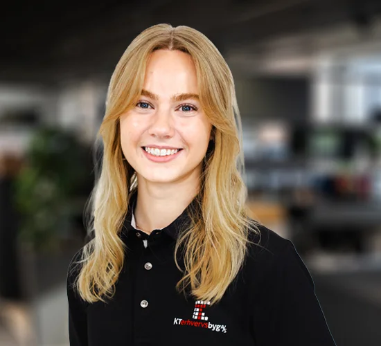 Smilende kvinde med langt blondt hår i sort polotrøje med logo fra KT Erhvervsbyg A/S