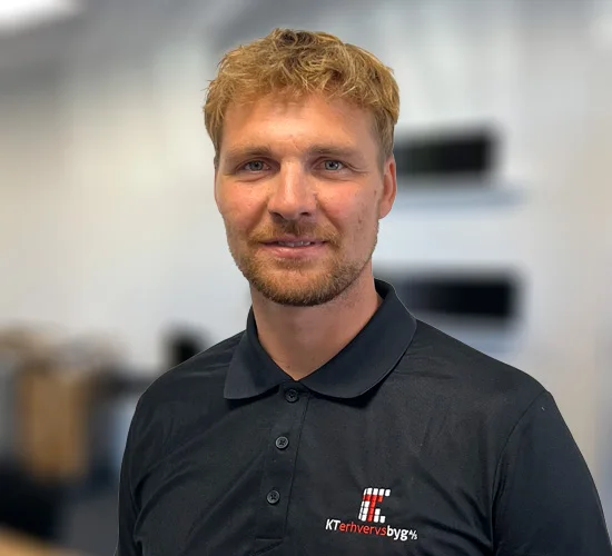 Mand med kort, lyst hår og skæg i mørk poloshirt med logo for KT Erhvervsbyg A/S