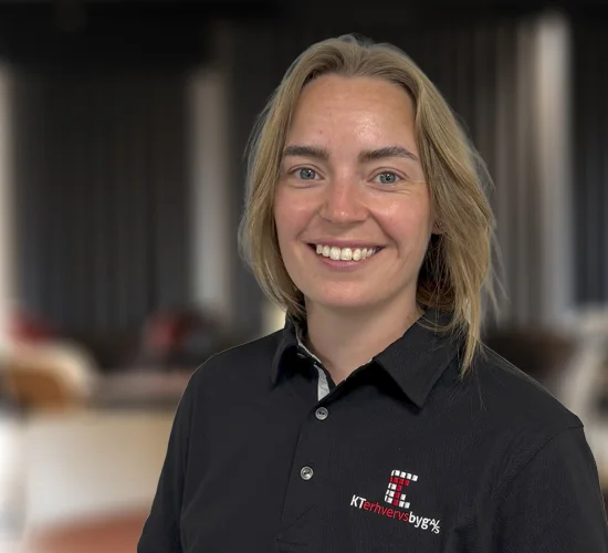 Smilende kvinde med lyst hår i sort poloshirt med logo fra KT Erhvervsbyg A/S