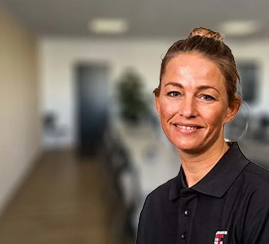 Portræt af en smilende kvinde med opsat hår og mørk poloshirt i et kontormiljø