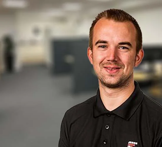 Smilende mand i sort poloshirt foran en sløret indendørs baggrund