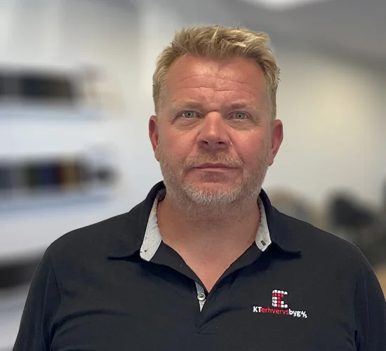 Portræt af en mand med kort lyst hår og skæg i mørk poloshirt med logo fra KT Erhvervsbyg A/S