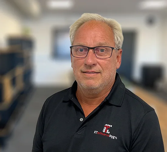 Mand med briller og sort polo med logo fra KT Erhvervsbyg A/S, fotograferet på et kontor