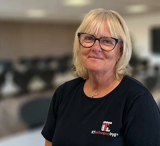 Kvinde med lyst hår og briller i sort T-shirt med logo for KT Erhvervsbyg A/S