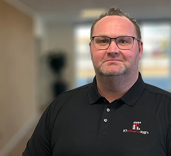 Portræt af en mand med briller og sort poloshirt med logo fra KT Erhvervsbyg A/S