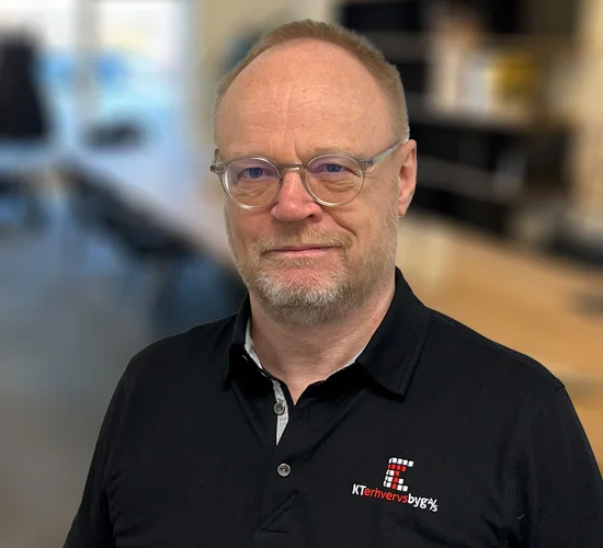 Mand med briller og kort skæg i sort poloshirt med logo for KT Erhvervsbyg A/S