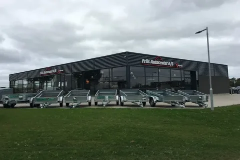 Friis Autocenter A/S' mørke bygning med store glaspartier og flere trailere parkeret foran