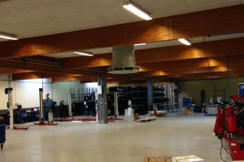 Stort autoværksted med lifte, dækreoler og rødt værkstedsudstyr under synlige træbjælker