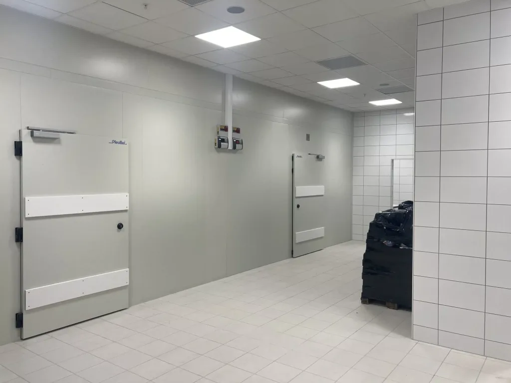 Flisebelagt rum med to store grå døre og en palle med sortindpakkede varer