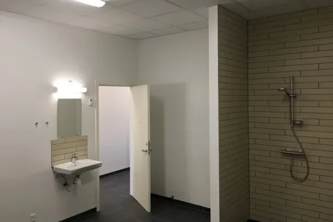 Badeværelse med håndvask, spejl og åben dør ved siden af en flisebeklædt bruseniche