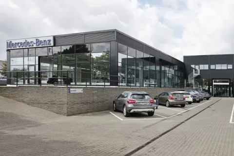 Mercedes-Benz-bilhus med stor glasfacade og parkerede biler foran
