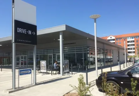 Lagkagehuset med glasfacade, udendørs siddepladser og skilt til drive-in