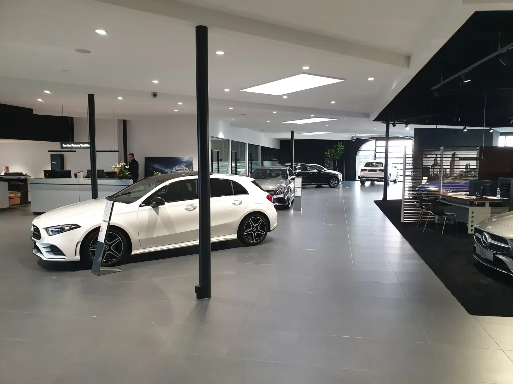 Lyst bilshowroom med flere udstillede biler, gråt klinkegulv og en receptionsskranke