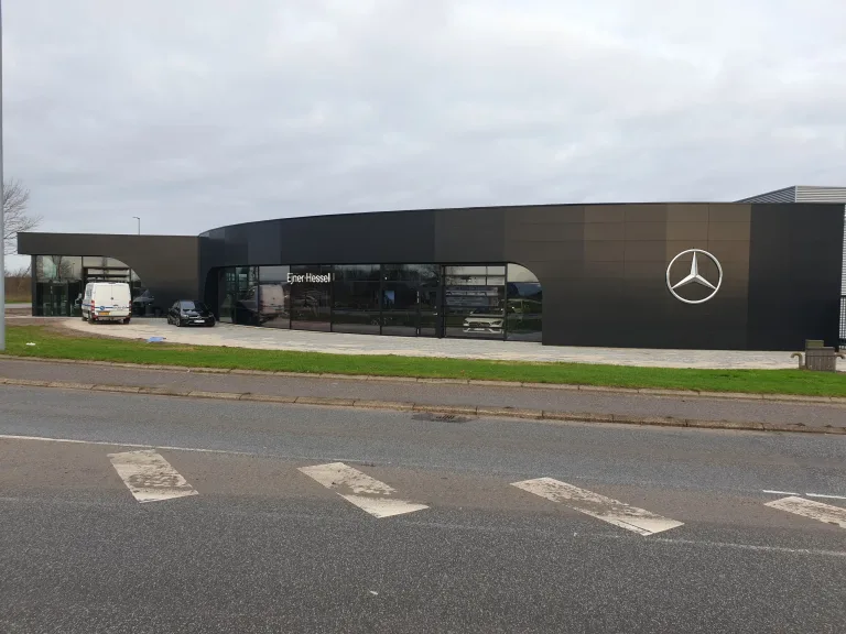 Ejner Hessels bilhus med mørk facade, store glaspartier, biler i udstillingen og en Mercedes-stjerne på væggen