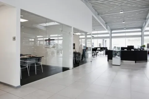 Lyst indgangsområde med glasafskærmet møderum, arbejdspladser og en sort receptionsskranke