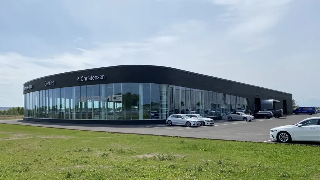 P. Christensens bilhus med buet glasfacade, mørk overetage og parkerede biler foran