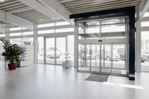 Lyst indgangsparti i bilhus med glasdøre, store vinduer og biler parkeret udenfor