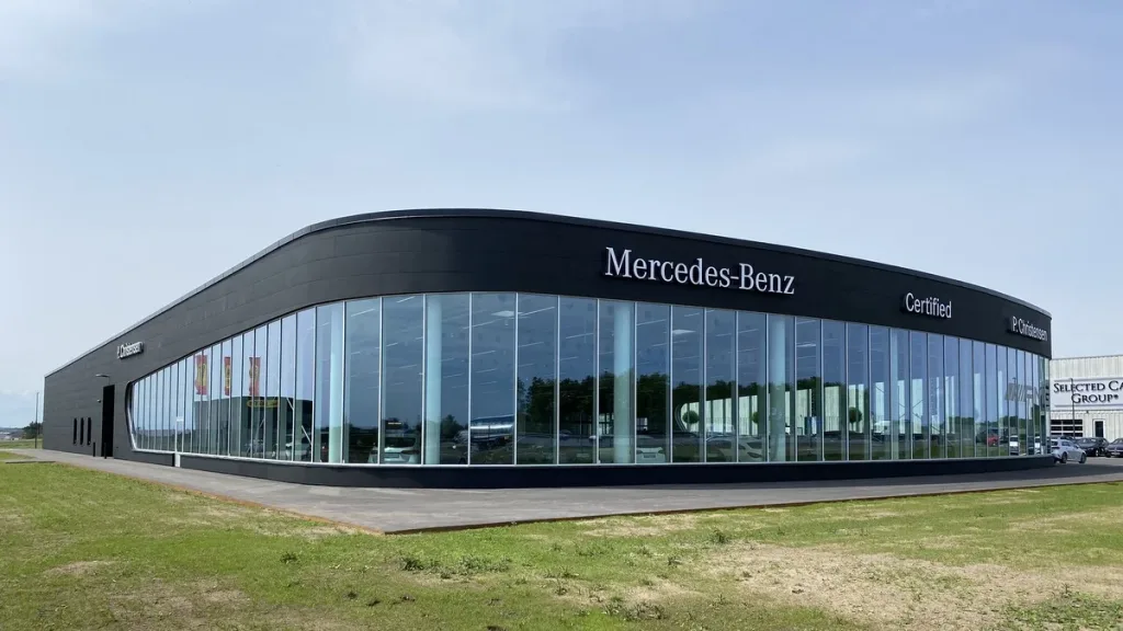 Bilhus med sort facade, store glaspartier og Mercedes-Benz-skilt. Biler ses gennem vinduerne