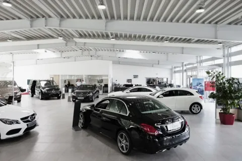 Lyst bilshowroom med flere udstillede biler, højt loft og synlige ståldragere