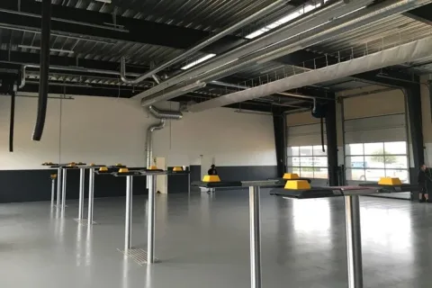 Stor værkstedshal med gråt gulv, ventilationskanaler, udstyr på søjler og to store porte
