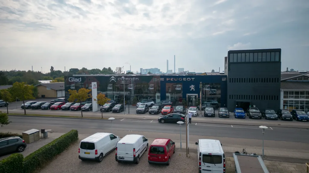 Bilcenter med Glad-, Citroën- og Peugeot-skilte på facaden og mange parkerede biler foran