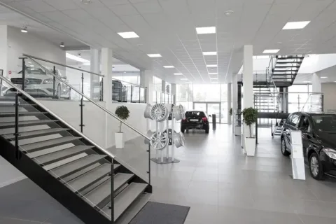 Lyst bilshowroom med udstillede biler, fælge på stativ og trappe med glasværn