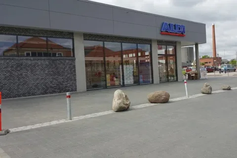 Aldi-butikkens facade med store glaspartier og indgang ud mod et flisebelagt areal med store sten