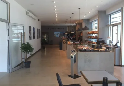 Lyst bageri med brød og kager i glasmontrer, caféborde og store vinduer