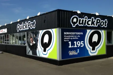 Sort QuickPot-bygning med store skilte, vinduer og facadegrafik om serviceeftersyn