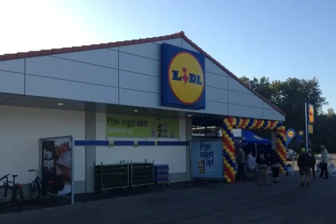 Lidl-butik med farverige balloner ved indgangen, indkøbsvogne og mennesker foran facaden
